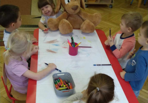 Dzieci siedzą przy stolikach kolorują wielkoformatowe pieski