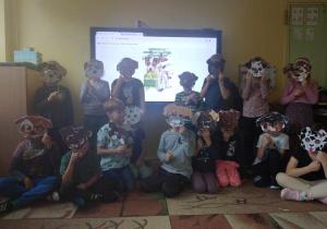 Dzieci z grupy zielonej pozują do zdjęcia grupowego trzymając maski kundelków
