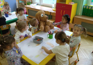 Dzieci siedzą przy stolikach kolorują wielkoformatowe pieski