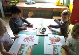 Dzieci siedzą przy stoliku, wyklejają brakujące elementy wiewiórki plasteliną