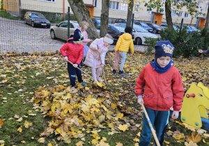 Chętne dzieci grabią liście w ogrodzie przedszkolnym.