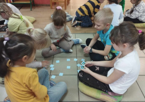 Dzieci siedzą w grupach i grają w menory.