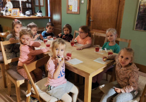 dzieci siedzą przy stolikach jedząc słodki poczęstunek