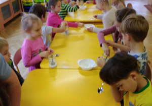 dzieci siedzą przy stołach prowadzą eksperymenty.
