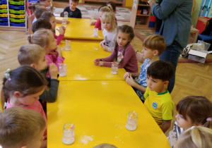dzieci siedzą przy stołach prowadzą eksperymenty.