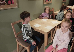 Dzieci siedzą przy stolikach, czekają na słodki poczęstunek.