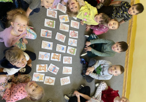 Dzieci siedzą na dywanie z ułożoną grą memory