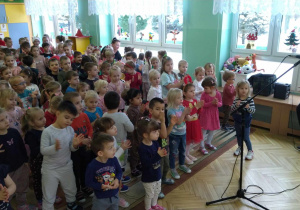 Dzieci stoją na dywanie, klaszcząc w rytm muzyki