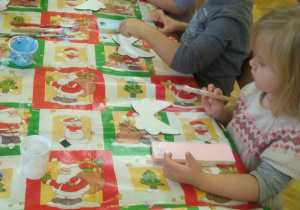 Dzieci siedzą przy stole, wykonują drewniane aniołki