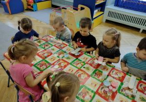 Dzieci siedzą przy stole, wykonują drewniane aniołki