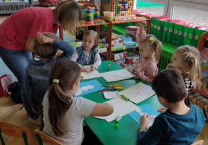 dzieci siedzą przy stoliku, wykonują bałwanka z papieru