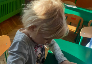 dziecko siedzi przy stoliku i z kół origami klei pingwina.