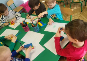 Dzieci siedzą przy stoliku obrysowują klocki lego