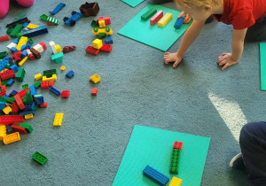 Dzieci siedzą na dywanie i bawią się klockami Lego