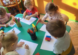Dzieci siedzą przy stoliku obrysowują klocki lego