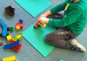 Chłopiec siedzi na dywanie i buduje z klocków