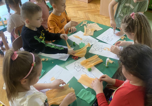 Dzieci siedzą przy stolikach, wykonują pracę plastyczną - marchewkę