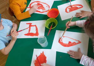 Dzieci siedzą przy stoliku, malują farbami marchewki