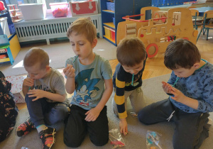Dzieci uczestniczą w ćwiczeniach oddechowych,przyciągając kostkę przez słomkę