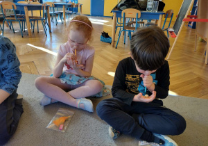 Dzieci uczestniczą w ćwiczeniach oddechowych,przyciągając kostkę przez słomkę