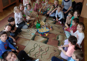 Dzieci siedzą na dywanie, w środku są pisanki, gałązki z ozdobami