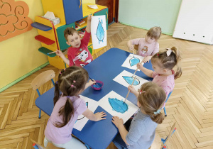 Dzieci siedzą przy stoliku, malują farbami kroplę wody