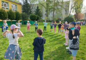 Dzieci stoją w kole, trener prezentuje chwyty karate.