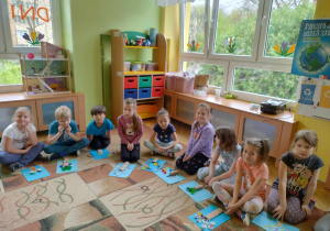dzieci siedzą na dywanie, prezentują swoje prace