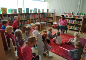 dzieci siedzą na krzesłach i dywanie, słuchają opowieści pani bibliotekarki