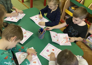 dzieci siedzą przy stolikach, wykonując ćwiczenia