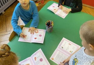 dzieci siedzą przy stolikach, wykonując ćwiczenia