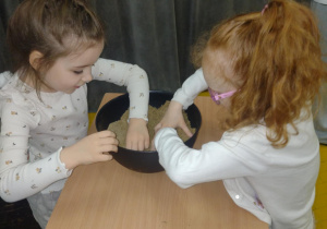 Dwie dziewczynki szukają w piasku ukrytego skarbu