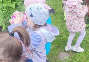 dzieci obserwują przyrodę przez eko-lornetkę w ogrodzie przedszkolnym