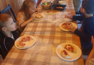 Dzieci jedzą przygotowane przez siebie pizze