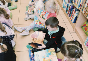 dzieci siedzą na poduchach, oglądają książki