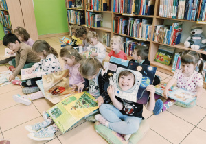 dzieci siedzą na poduchach, oglądają książki