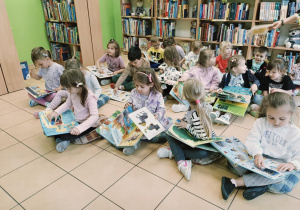 dzieci siedzą na poduchach, oglądają książki