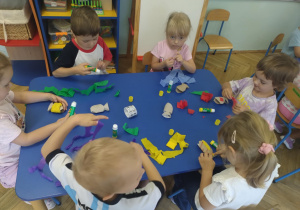 Dzieci siedzą przy stolikach i wykonują pracę plastyczną"Kolorowe rybki" przy użyciu materiałów z recyklingu, bibuły, kleju i gotowych oczek.