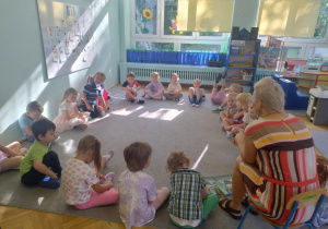 Dzieci siedzą w kole na dywanie a prowadząca czyta książkę pt. "Trzy życzenia".