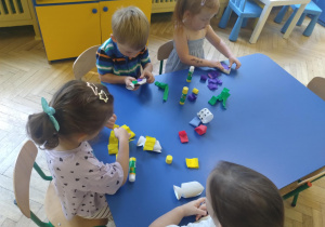 Dzieci siedzą przy stolikach i wykonują pracę plastyczną"Kolorowe rybki" przy użyciu materiałów z recyklingu, bibuły, kleju i gotowych oczek.