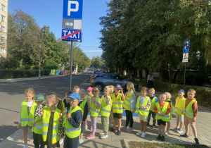 Dzieci stoją na chodniku pod znakiem „Parking”