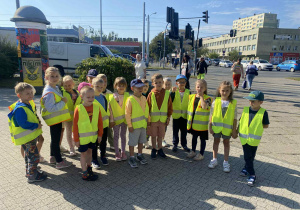 Dzieci stoją na chodniku pod znakiem „ nakaz skrętu w prawo” , „ Ustąp pierwszeństwa przejazdu „