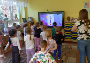 prowadząca objaśnia dzieciom wykonanie zadania na monitorze edukacyjnym