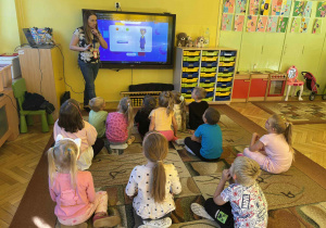 prowadząca objaśnia dzieciom wykonanie zadania na monitorze edukacyjnym