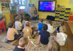 prowadząca objaśnia dzieciom wykonanie zadania na monitorze edukacyjnym
