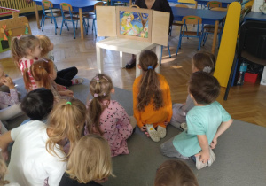 dzieci siedząc na dywanie oglądają bajkę w teatrzyku kamishibai
