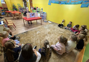 dzieci siedząc na dywanie oglądają bajkę w teatrzyku kamishibai