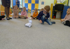 Chłopiec kuca przy robocie i głaszcząc go po głowie uruchamia photona-robota Franka
