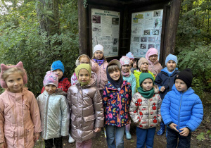 dzieci pozują do zdjęcia przy tablicy edukacyjnej w lesie