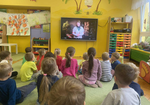 dzieci siedzą na dywanie oglądając film